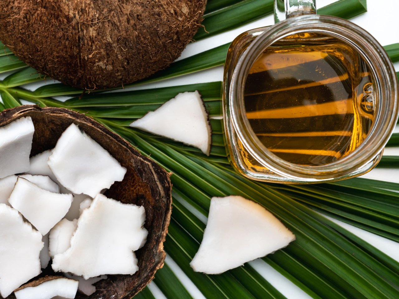 A beautifully arranged coconut half with glistening coconut oil pouring from it, surrounded by fresh green palm leaves and a serene beach background, capturing the essence of a tropical paradise.